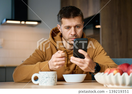 Man checking smartphone while eating breakfast at home Man checking smartphone while eating breakfast at home 139219351
