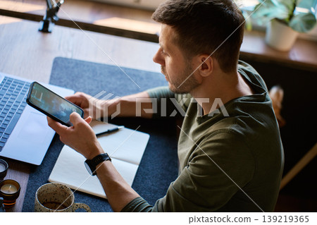 Man checking unknown caller on smartphone at desk 139219365