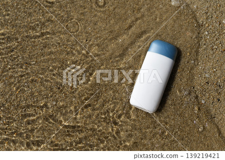 White skincare product bottle with blue cap on wet beach sand and clear water 139219421