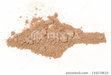Spilled cocoa powder with small lumps, forming an uneven textured spot on a white background. Spilled cocoa powder with small lumps, forming an uneven textured spot on a white background. 139219618