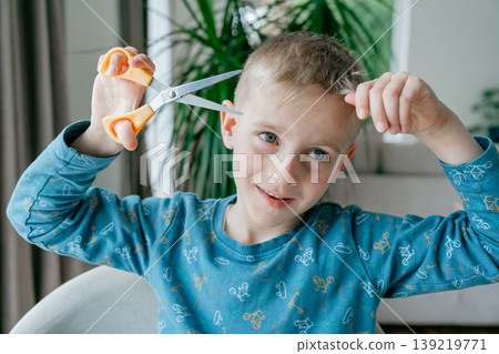 Child stretching scissors with both hands. Concept of curiosity, play, and safety awareness in everyday home life. 139219771