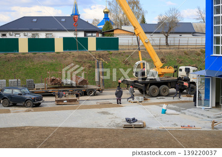 Mobile crane next to a blue building under construction at a construction site during work. Frame of the building under construction in the spring. 139220037