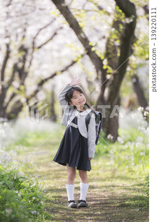 A young girl, newly enrolled in school, raises her hand on a street lined with cherry trees. A young girl, newly enrolled in school, raises her hand on a street lined with cherry trees. 139220111