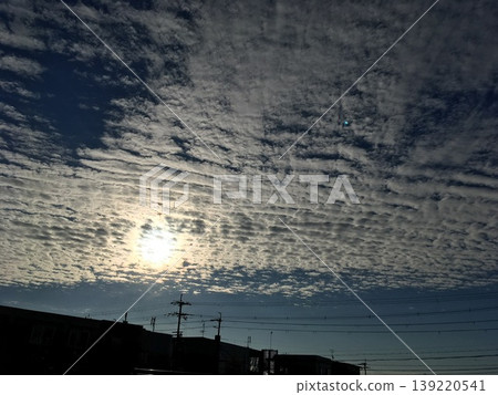 A landscape of cirrocumulus clouds shimmering in the morning sun and the silhouettes of a residential area. 139220541