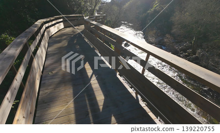 Sunlit Wooden Boardwalk Overlooking a Rushing River in a Natural Valley Sunlit Wooden Boardwalk Overlooking a Rushing River in a Natural Valley 139220755