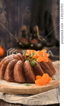 Golden brown bundt cake garnished with fresh tangerine segments and mint on a rustic wooden board Golden brown bundt cake garnished with fresh tangerine segments and mint on a rustic wooden board 139220763