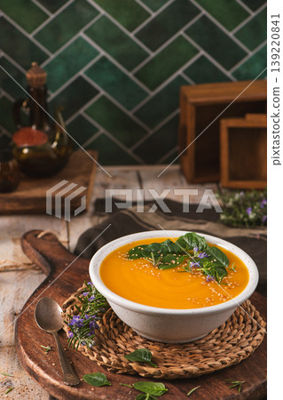 Creamy Pumpkin Soup with Fresh Herbs and Sesame Seeds in a Rustic Kitchen Setting 139220841
