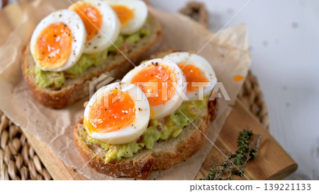 Soft Boiled Eggs on Smashed Avocado Toast with Black Pepper and Herbs 139221133