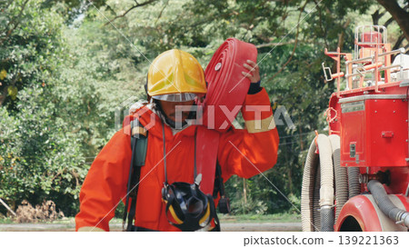 Fireman prepare equipment at fire engine truck. Man hand connect water tube with fire truck fighting extinguisher. Firefighter using fire hose, tube, chemical water foam spray police rescue training Fireman prepare equipment at fire engine truck. Man hand connect water tube with fire truck fighting extinguisher. Firefighter using fire hose, tube, chemical water foam spray police rescue training 139221363