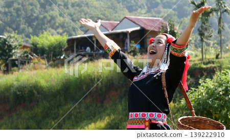 Smiling tribal woman in traditional colorful dress raising arms with joy in rural village, celebrating culture, happiness, and ethnic lifestyle in nature 139222910