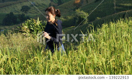 Asian woman jogging through lush rice fields on a mountain during sunrise, enjoying nature, health, and rural lifestyle in an agricultural environment 139222913