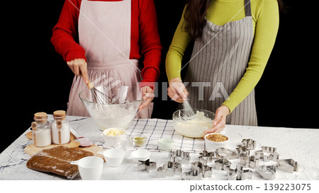 Two people preparing cookie dough together, whisking ingredients in glass bowls surrounded by baking tools and cutters; warm homemade baking atmosphere and collaborative kitchen Two people preparing cookie dough together, whisking ingredients in glass bowls surrounded by baking tools and cutters; warm homemade baking atmosphere and collaborative kitchen 139223075