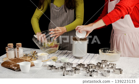 Bakers transferring cookie dough and ingredients into bread maker or dough mixer during recipe video shoot, surrounded by baking tools and cookie cutters Bakers transferring cookie dough and ingredients into bread maker or dough mixer during recipe video shoot, surrounded by baking tools and cookie cutters 139223135