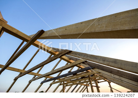 New wooden house under construction. Close-up of attic roof frame against clear sky from inside. Ecological dream home of natural materials. Building, construction and renovation concept. New wooden house under construction. Close-up of attic roof frame against clear sky from inside. Ecological dream home of natural materials. Building, construction and renovation concept. 139224207