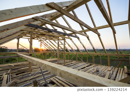 New wooden house under construction. Close-up of attic roof frame against clear sky from inside. Ecological dream home of natural materials. Building, construction and renovation concept. New wooden house under construction. Close-up of attic roof frame against clear sky from inside. Ecological dream home of natural materials. Building, construction and renovation concept. 139224214