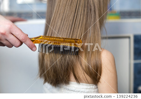 Mother hand with brush combing long fair hair of cute child girl after bath on blurred interior background. Mother hand with brush combing long fair hair of cute child girl after bath on blurred interior background. 139224236