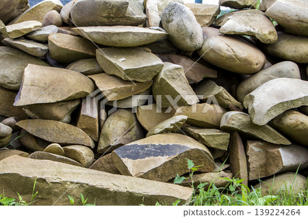 Lit by sun pile of big crackled different sizes and shapes light soft brown stones on green grass. Natural resources, building material, construction and decoration concept. Lit by sun pile of big crackled different sizes and shapes light soft brown stones on green grass. Natural resources, building material, construction and decoration concept. 139224264