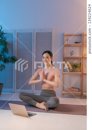 A woman doing yoga while looking at her computer in her room. A woman doing yoga while looking at her computer in her room. 139224624