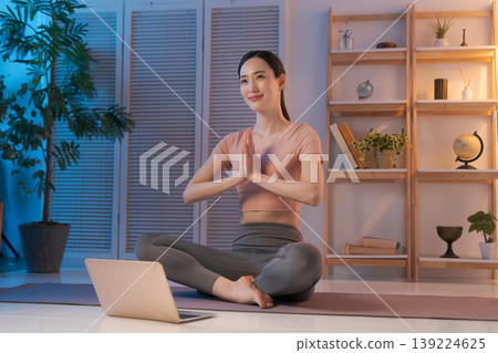 A woman doing yoga while looking at her computer in her room. A woman doing yoga while looking at her computer in her room. 139224625