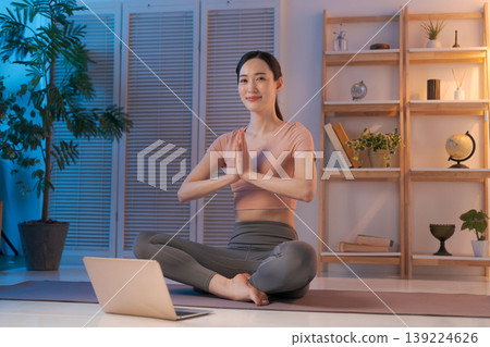 A woman doing yoga while looking at her computer in her room. A woman doing yoga while looking at her computer in her room. 139224626