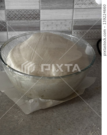 Fresh dough covered and rising in a kitchen setting. Fresh dough covered and rising in a kitchen setting. 139224660