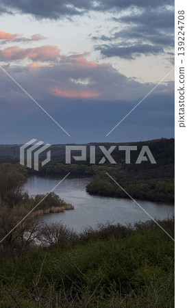 Tranquil river view with lush greenery and vibrant clouds. 139224708