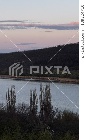 Tranquil river scene featuring trees and gentle hills. Tranquil river scene featuring trees and gentle hills. 139224710