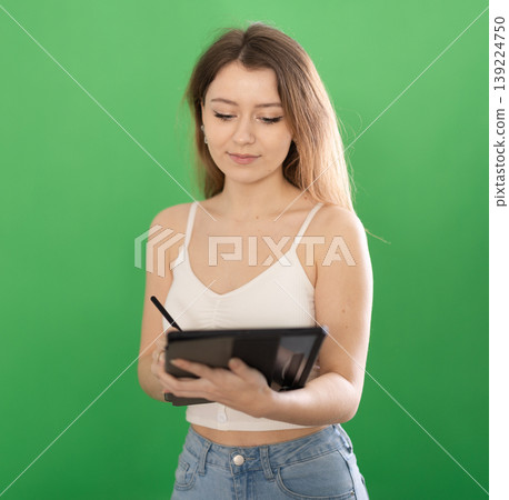 Young woman taking notes on tablet in front of green screen Young woman taking notes on tablet in front of green screen 139224750