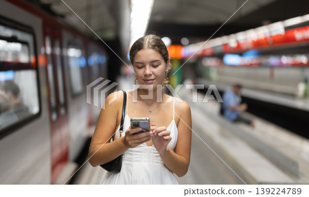 Young woman standing on platform near train with mobile phone Young woman standing on platform near train with mobile phone 139224789