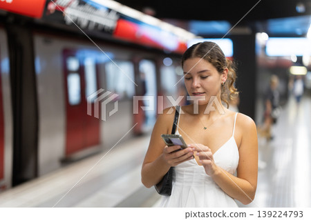 Young girl standing on metro platform with phone in hand Young girl standing on metro platform with phone in hand 139224793