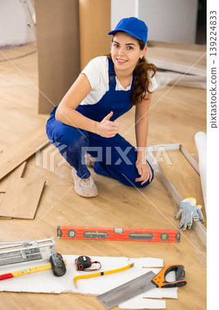 Young woman builder making thumb up gesture while installing parquet Young woman builder making thumb up gesture while installing parquet 139224833