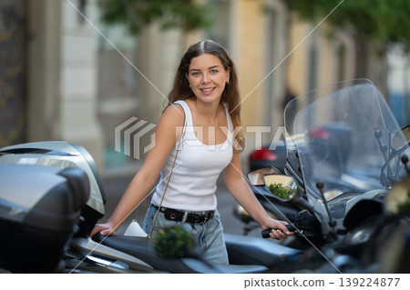 Young tourist girl looking at parked motorbikes on city street Young tourist girl looking at parked motorbikes on city street 139224877