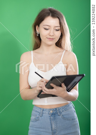 Young woman taking notes on tablet in front of green screen Young woman taking notes on tablet in front of green screen 139224882