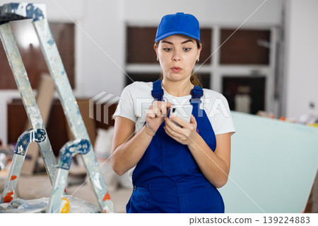 Female construction worker using smartphone in apartment 139224883