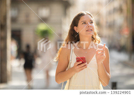 Young woman with phone walking along city street Young woman with phone walking along city street 139224901