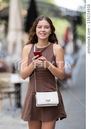 Positive young woman watching her smartphone when walking in street of Barcelona, lifestyle technology concept 139224916