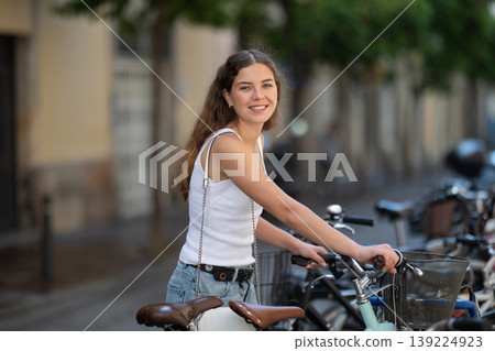 Young girl parks her bicycle on street after walking around city Young girl parks her bicycle on street after walking around city 139224923