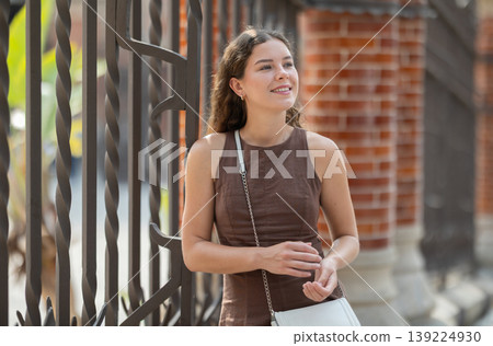Pretty young woman traveler in summer dress with handbag posing near Hospital de la Santa Creu i Sant Pau in Barcelona on spring day 139224930