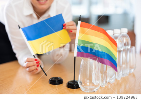 Young woman puts flags of Ukraine and LGBT on table in office 139224965