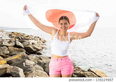 Enjoying vacation in Japan. Young woman with national Japanese flag on the seashore on sunny day 139224987