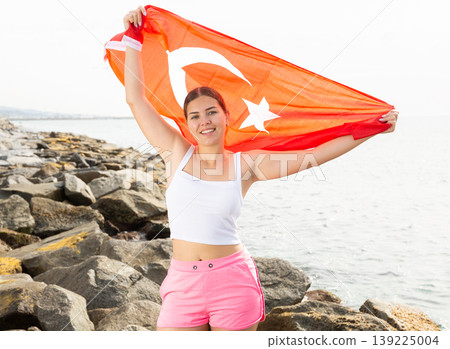 Enjoying vacation in Turkey. Young woman with national Turkish flag on the seashore on sunny day Enjoying vacation in Turkey. Young woman with national Turkish flag on the seashore on sunny day 139225004