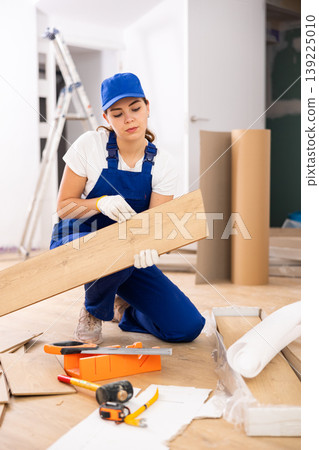 Woman builder puts laminate on the floor in room 139225010