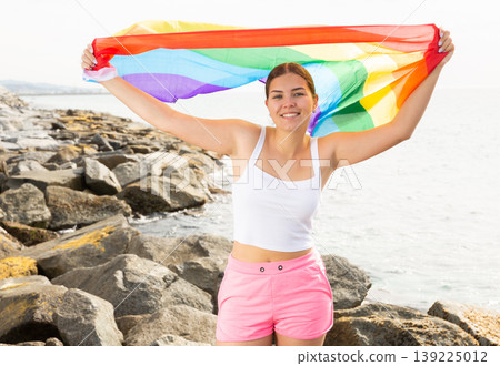 Portrait of a playful girl holding an LGBT flag in her hands on the beach on sunny day Portrait of a playful girl holding an LGBT flag in her hands on the beach on sunny day 139225012