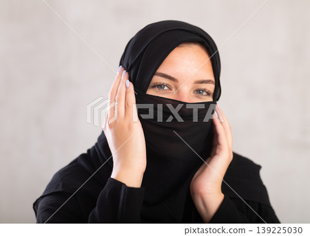 Muslim woman with face covered with burka holds thin fabric of yashmak with her hands Muslim woman with face covered with burka holds thin fabric of yashmak with her hands 139225030