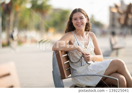Portrait of girl relaxing on bench in summer city park Portrait of girl relaxing on bench in summer city park 139225041