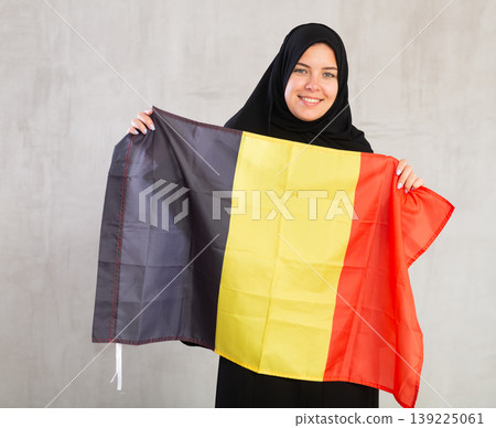 smiling Muslim woman in traditional black hijab holds flag of Belgium smiling Muslim woman in traditional black hijab holds flag of Belgium 139225061