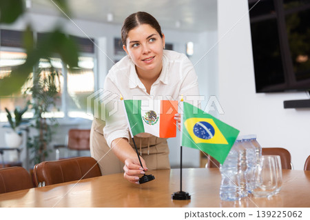 Young female assistant putting up brazilian and mexican flags on table for international negotiations Young female assistant putting up brazilian and mexican flags on table for international negotiations 139225062