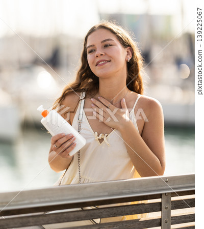 Young woman applying sunscreen on bench near port 139225067