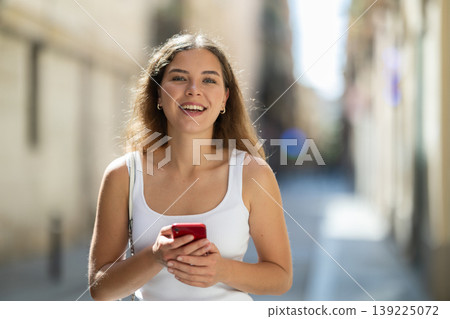 Young woman checking phone while walking in summer city Young woman checking phone while walking in summer city 139225072