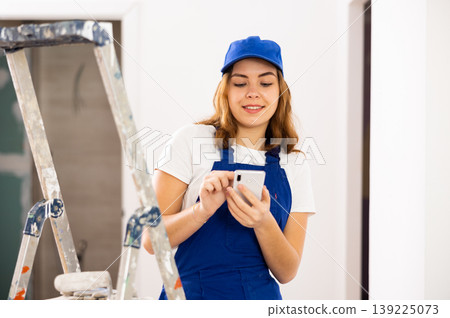 Positive young female contractor chatting online on smartphone Positive young female contractor chatting online on smartphone 139225073